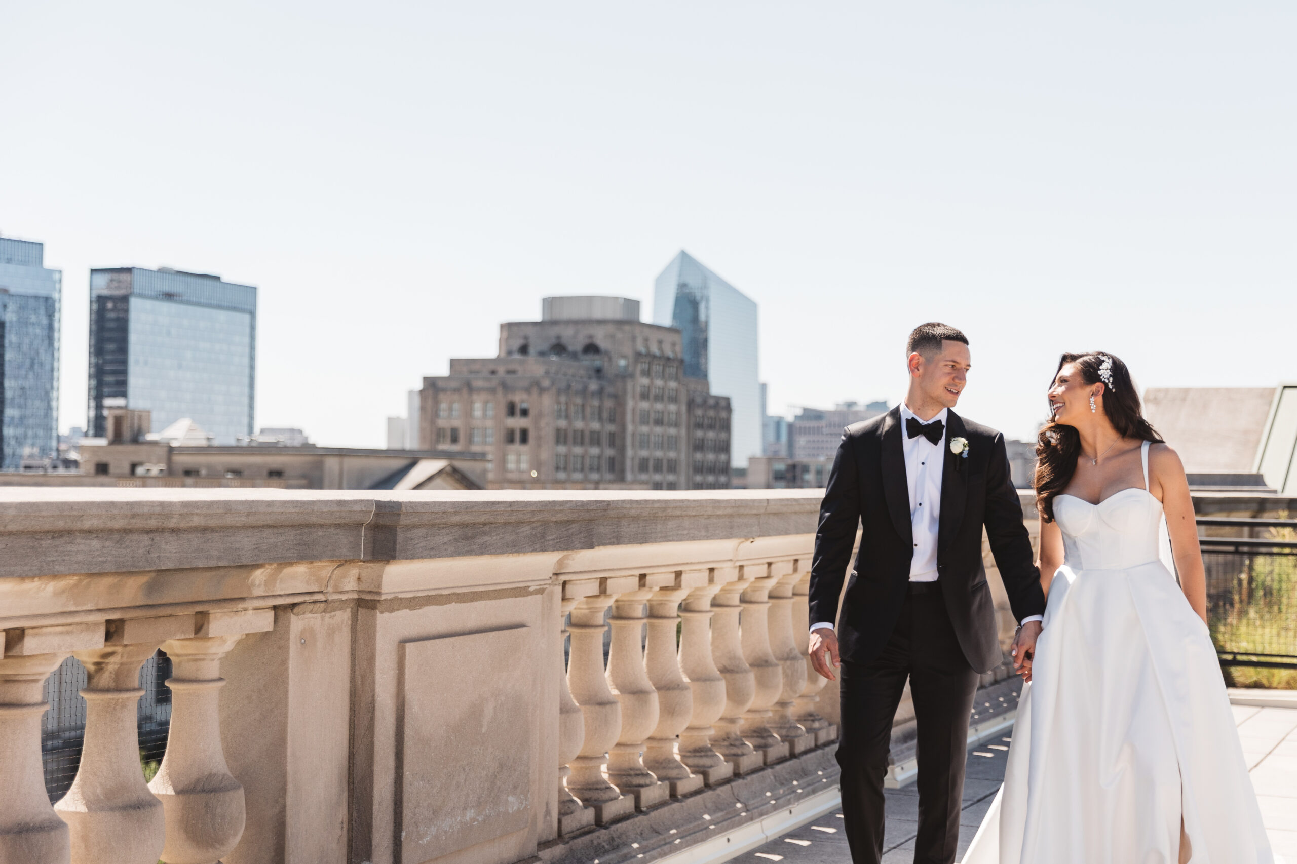 Alexa and Nicholas celebrate their wedding day with portraits on the rooftop of The Free Library of Philadelphia. The couple smiles with the view of the Philadelphia skyline behind them. Taken by Philadelphia Wedding Photographer Madison Neumann Photography.