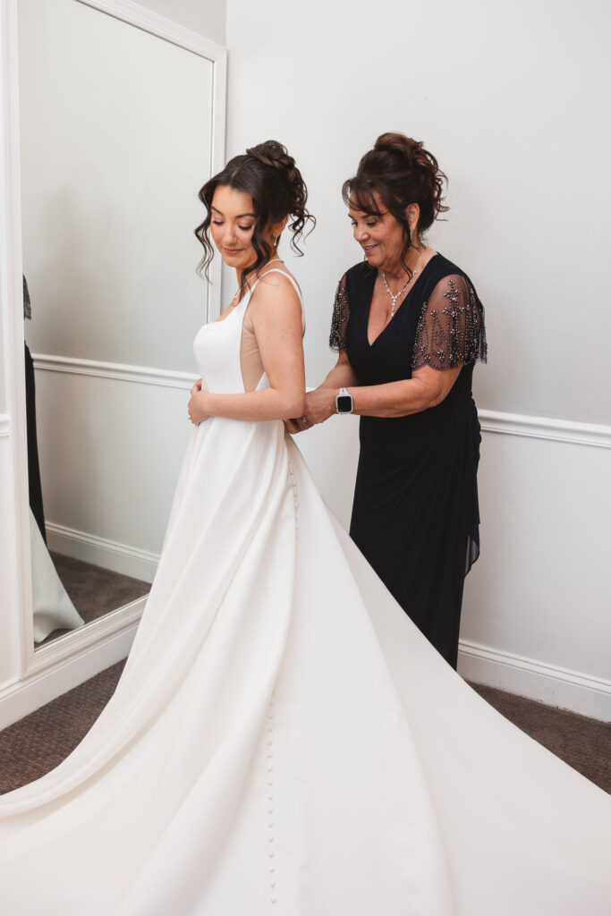 Brides mom zips her dress as she gets ready for her wedding day, wearing a veil and gown. Wedding day at Downingtown Country Club in Downingtown, PA. Photographed by South Jersey, Philadelphia based wedding photographer Madison Neumann Photography.