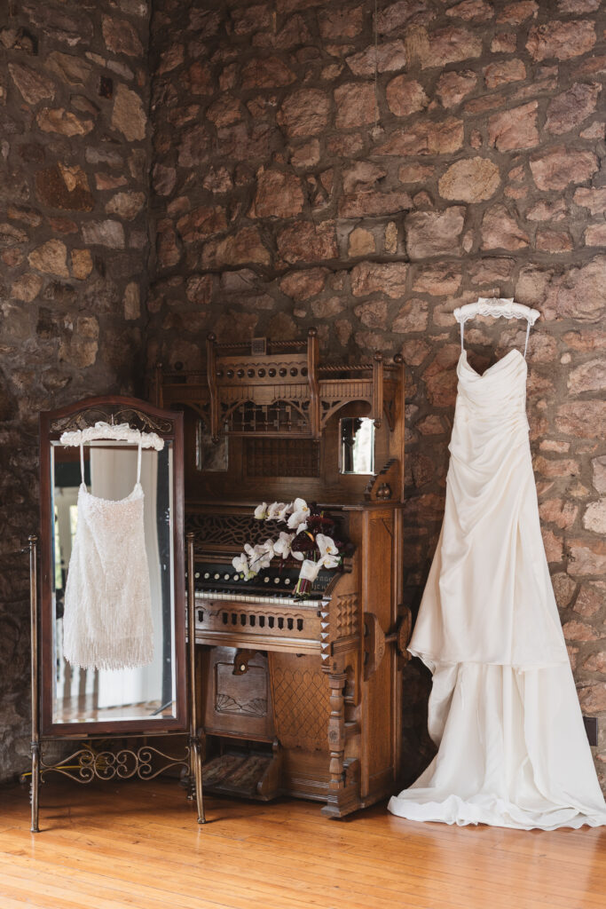 A wedding dress and after party dress hang next to a grand piano at Hollyhedge Estate in New Hope, PA. Taken by Pennsylvania wedding photographer Madison Neumann Photography.