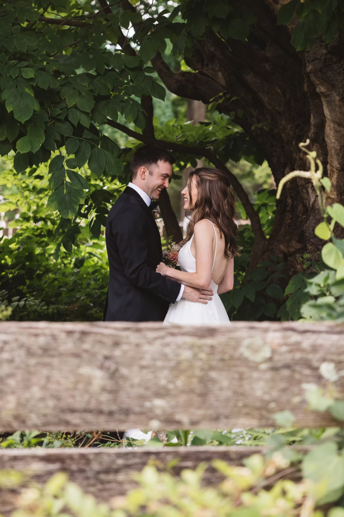 Bride and groom smile beneath trees after first look for wedding at Bartram's Garden in Philadelphia, PA. Photographed by South Jersey Philly wedding photographer Madison Neumann Photography.