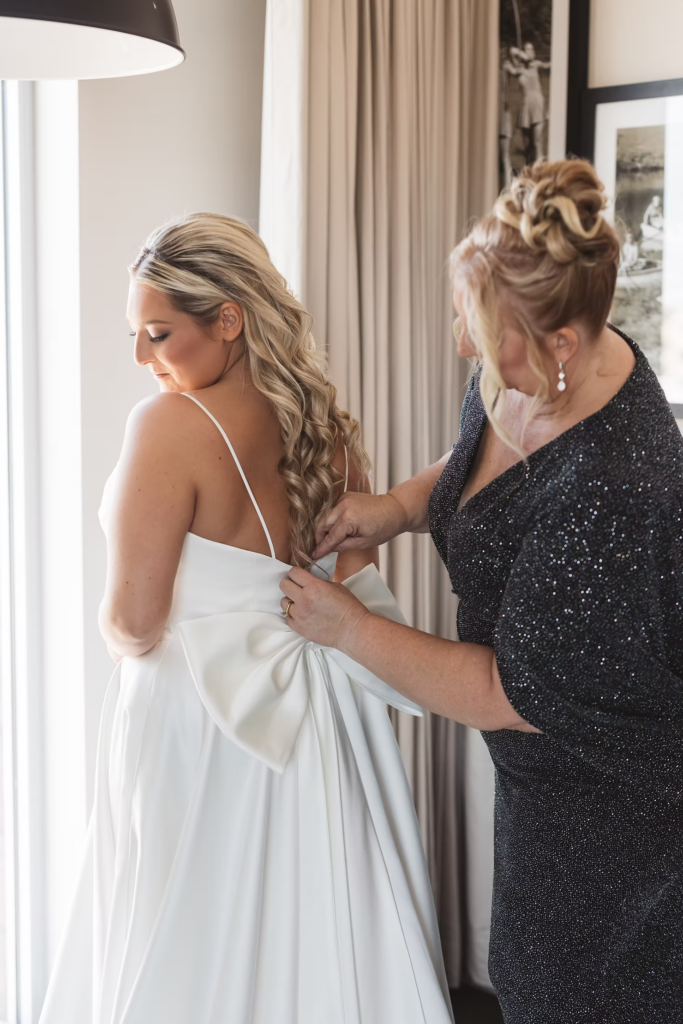 Bride in gown with bow on back, getting ready with mother for wedding day at The Ivy at Ellis Preserve in Newtown Square, Pennsylvania. Photographed by NJ, PA region wedding photographer Madison Neumann Photography.