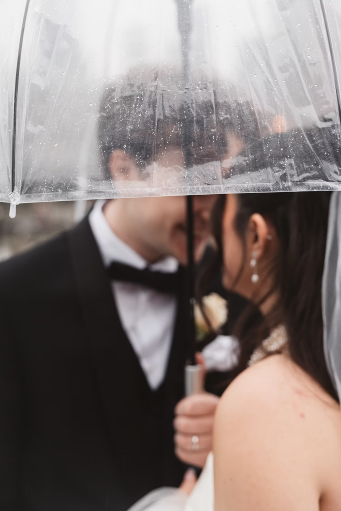 Bride and groom together outside in the rain under clear umbrella. Wedding day at Maritime Parc in Jersey City, NJ. Photographed by South Jersey, Philadelphia based wedding photographer Madison Neumann Photography.