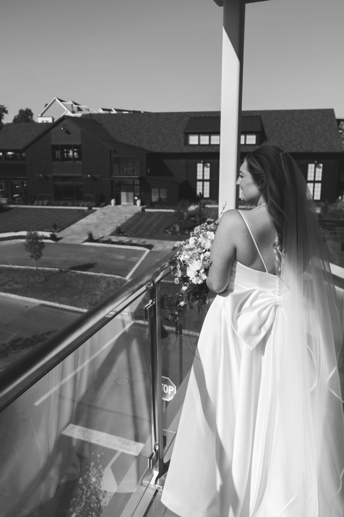 Black and white portrait of bride in gown and veil, holding bouquet on balcony. Photographed by wedding photographer Madison Neumann Photography for wedding day at The Ivy at Ellis Preserve in Newtown Square, Pennsylvania.