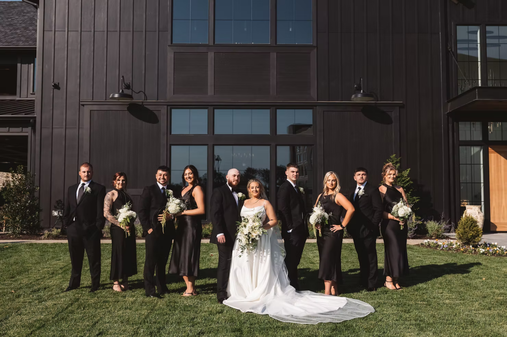Bride and groom pose with wedding party for outdoor portrait in the sun. Black and white attire color palette. Photographed by NJ/PA wedding photographer Madison Neumann Photography for wedding day at The Ivy at Ellis Preserve in Newtown Square, Pennsylvania.