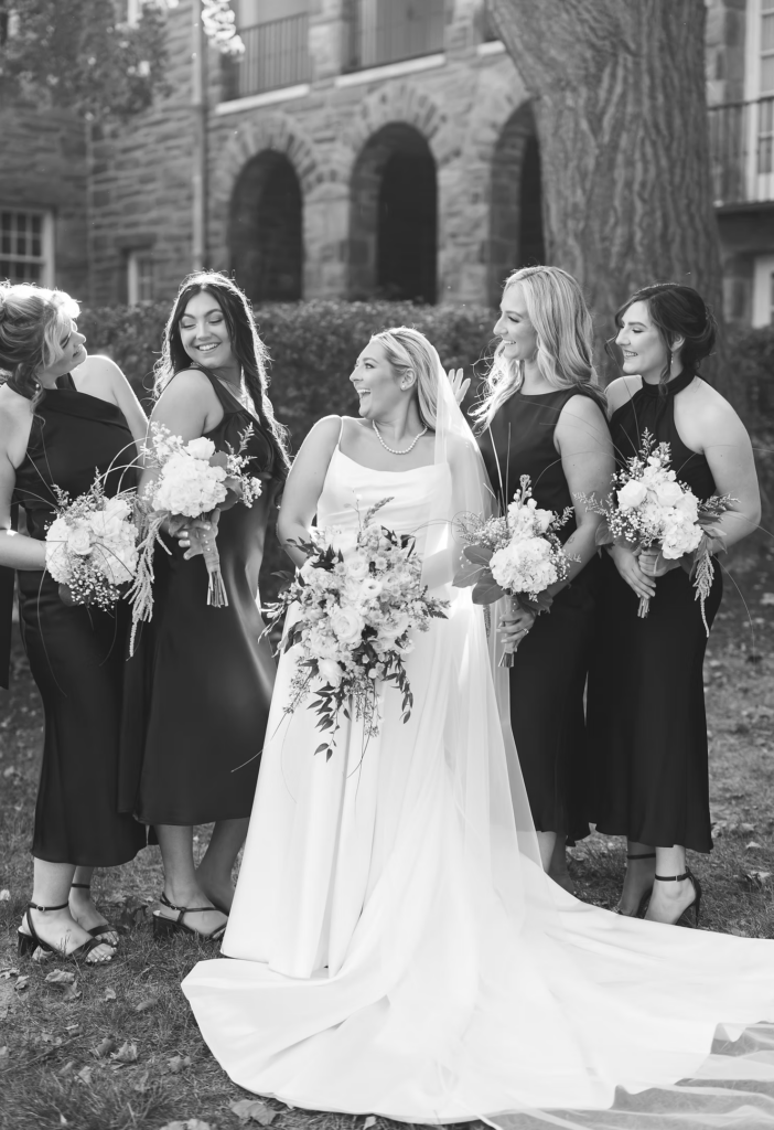 Black and white portrait of bride smiling with bridesmaids on her wedding day at The Ivy at Ellis Preserve by Finley Catering in Newtown Square, PA. Photographed by South Jersey, Pennsylvania region wedding photographer Madison Neumann Photography.