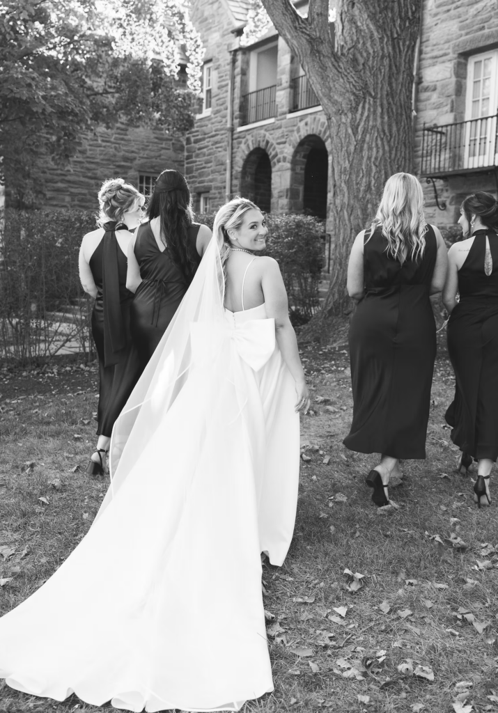 Bride in gown with bow and long veil smiling with bridal party on her wedding day at The Ivy at Ellis Preserve in Newtown Square, Pennsylvania. Photographed by NJ, PA region wedding photographer Madison Neumann Photography.