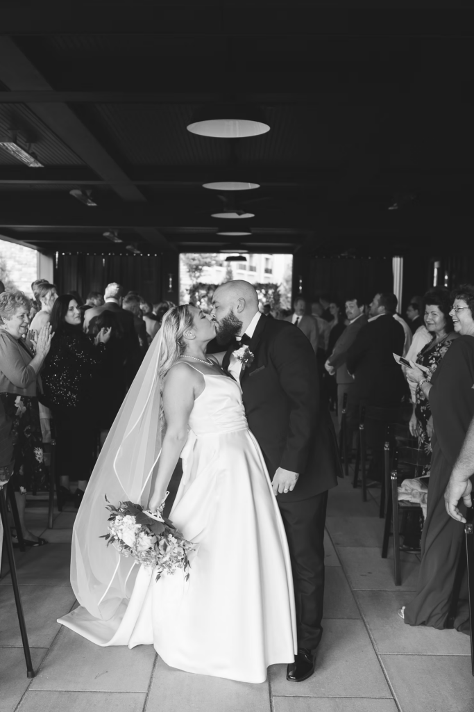 Black and white portrait of newlywed bride and groom at end of the aisle exiting ceremony on wedding day at The Ivy at Ellis Preserve by Finley Catering in Newtown Square, Pennsylvania. Photographed by NJ, PA region wedding photographer Madison Neumann Photography.
