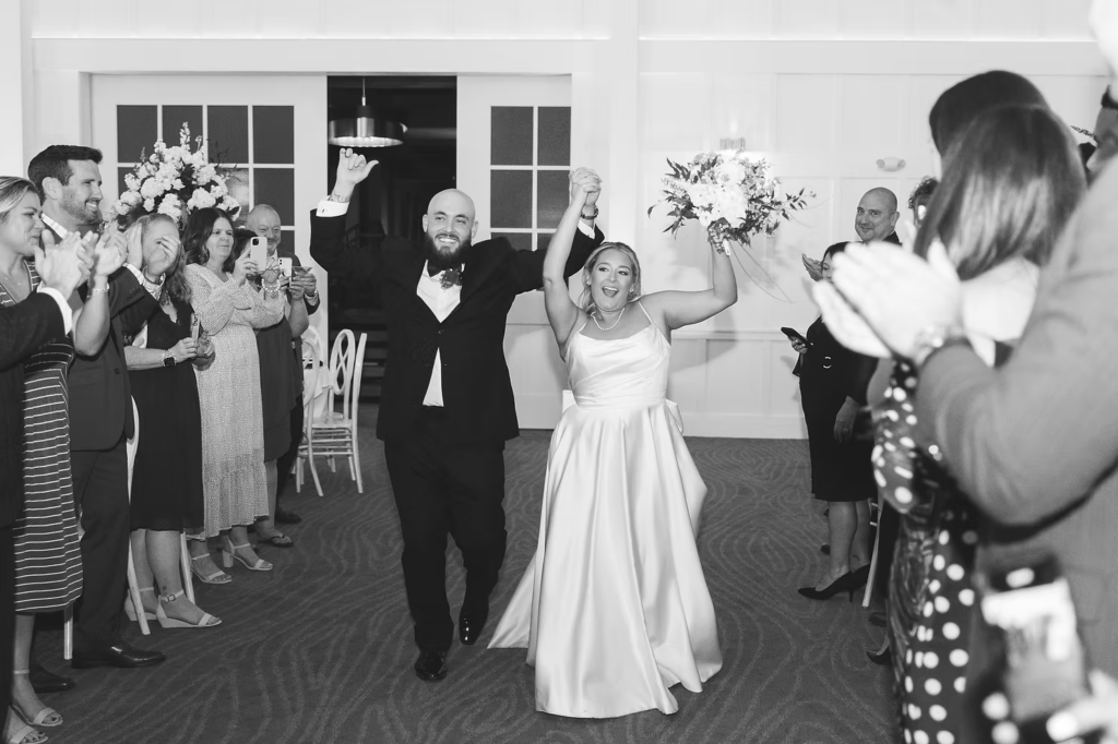Black and white portrait of newlywed bride and groom celebrating as they make their grand entrance during wedding reception at The Ivy at Ellis Preserve by Finley Catering in Newtown Square, PA. Wedding day photographed by South Jersey, Pennsylvania region wedding photographer Madison Neumann Photography.