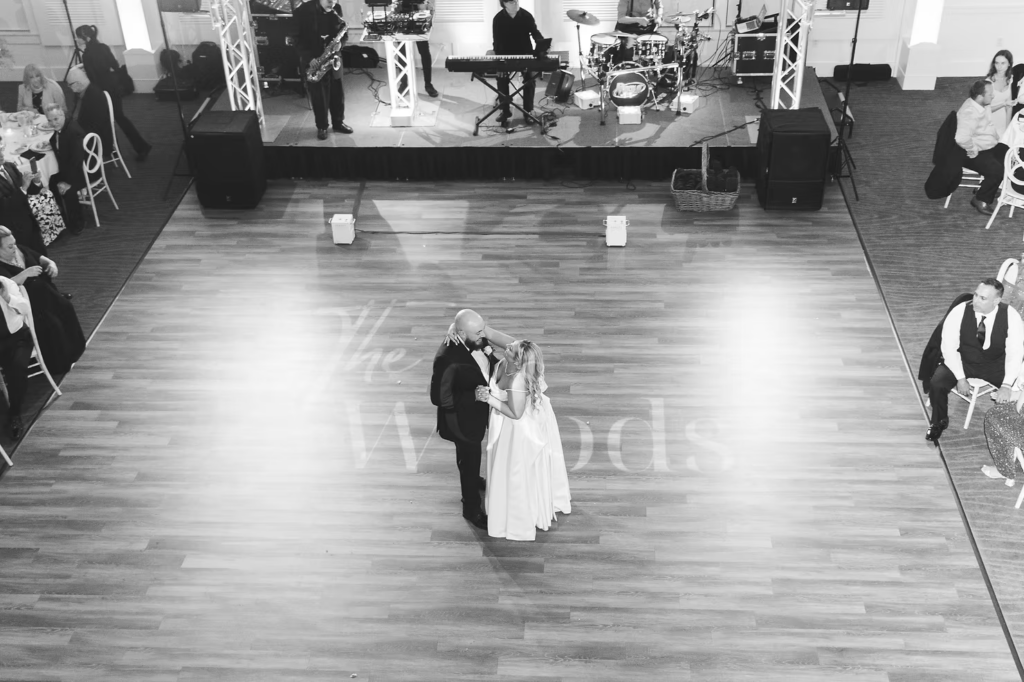 Black and white wide shot photograph of bride and groom sharing first dance during wedding reception at The Ivy at Ellis Preserve by Finley Catering in Newtown Square, PA. Wedding day photographed by South Jersey, Pennsylvania region wedding photographer Madison Neumann Photography.