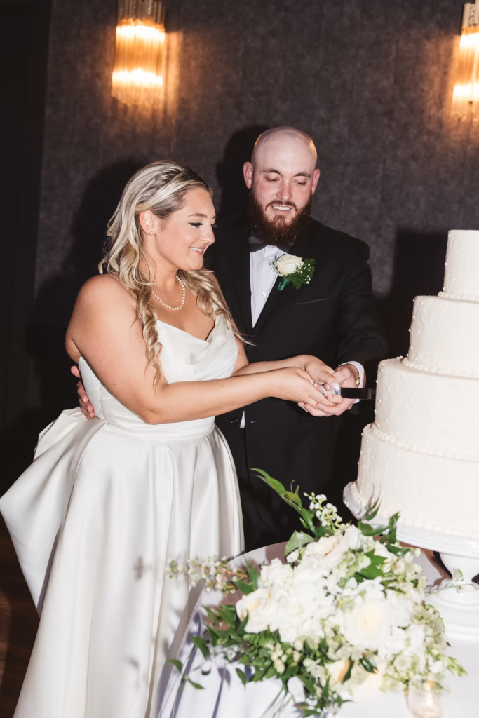 Flash photography portrait of bride and groom cutting layered cake wedding reception at The Ivy at Ellis Preserve by Finley Catering in Newtown Square, PA. Wedding night photographed by South Jersey, Pennsylvania region wedding photographer Madison Neumann Photography.