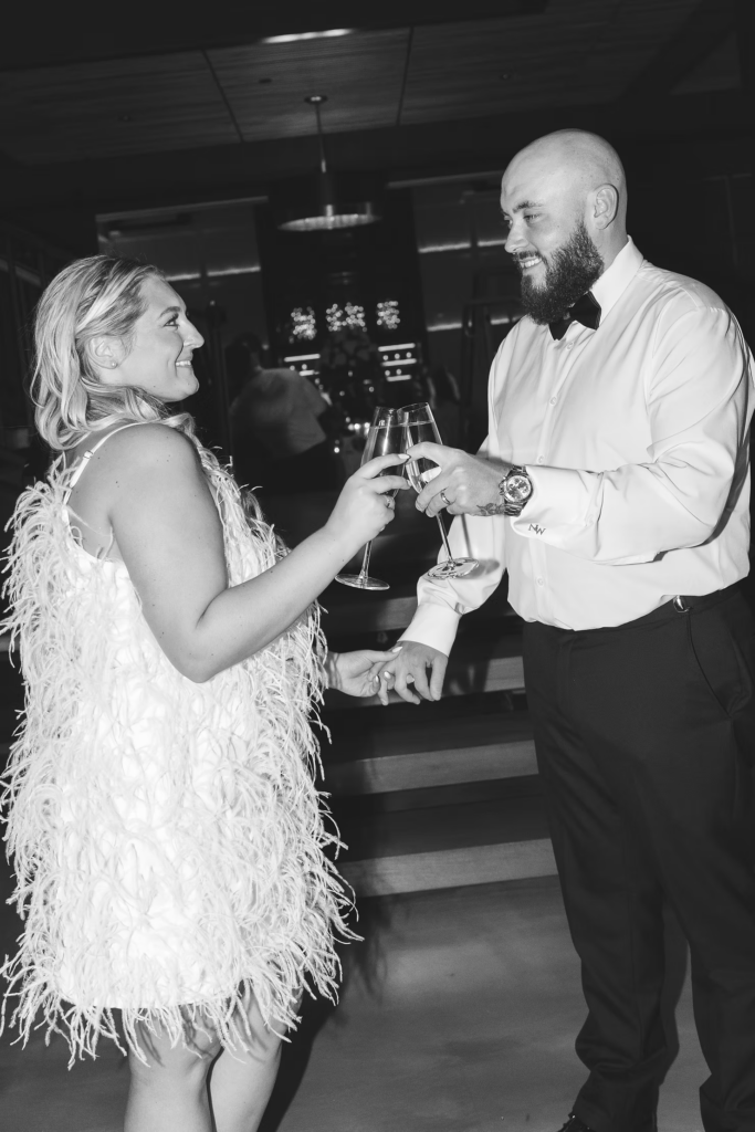 Black and white flash photography portrait of newlywed bride and groom cheering with champagne at end of the night for wedding reception at The Ivy at Ellis Preserve by Finley Catering in Newtown Square, PA. Wedding night photographed by South Jersey, Pennsylvania region wedding photographer Madison Neumann Photography.