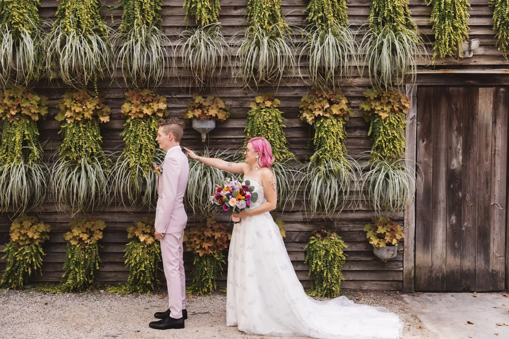 Bride and groom portrait at their first look at at their colorful garden party wedding at terrain in glen mills, PA. their first look is happening in front of a plant wall on the property, wooden and covered in green plants. Taken by philly wedding photographer Madison Neumann Photography.