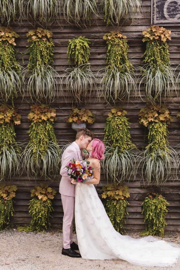 Bride and groom portrait at their first look at at their colorful garden party wedding at terrain in glen mills, PA. their first look is happening in front of a plant wall on the property, wooden and covered in green plants. Taken by philly wedding photographer Madison Neumann Photography.
