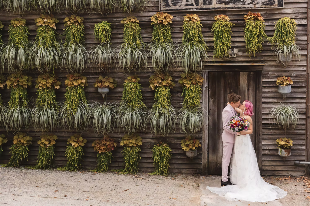 Bride and groom portrait at their first look at at their colorful garden party wedding at terrain in glen mills, PA. their first look is happening in front of a plant wall on the property, wooden and covered in green plants. Taken by philly wedding photographer Madison Neumann Photography.