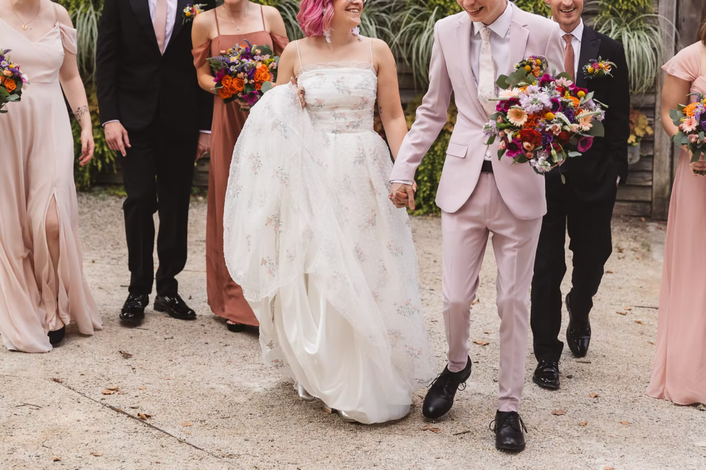 Wedding party photo at Terrain in Glen Mills, PA. Taken in front of a plant wall on the property, wooden and covered in green plants. The wedding party wears mismatched shades of pink. Taken by philly wedding photographer Madison Neumann Photography.