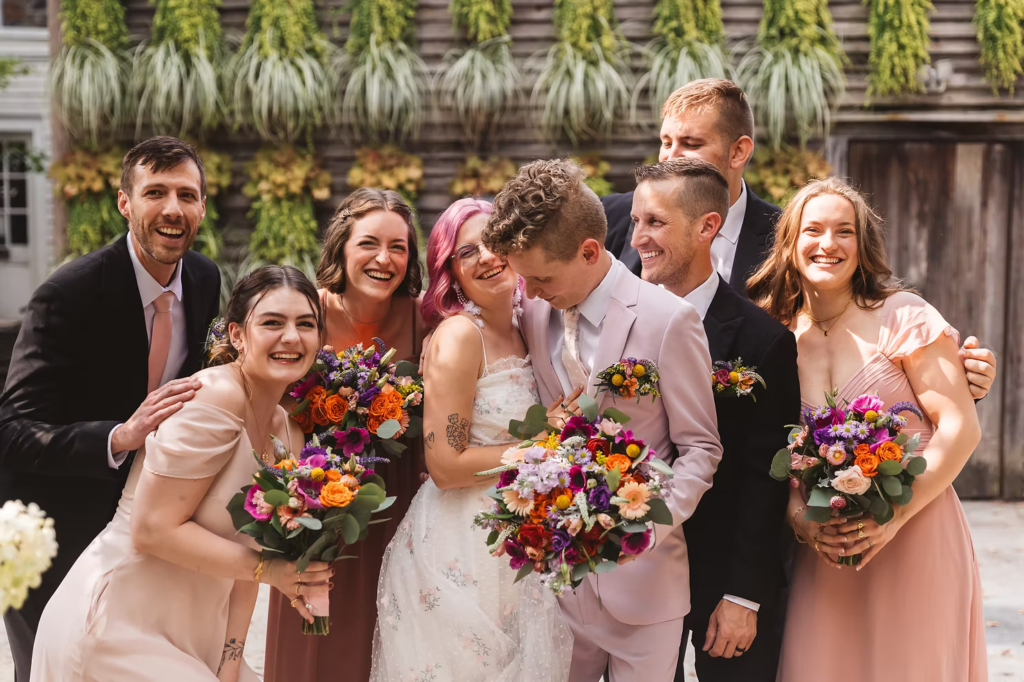 Wedding party photo at Terrain in Glen Mills, PA. Taken in front of a plant wall on the property, wooden and covered in green plants. The wedding party wears mismatched shades of pink. Taken by philly wedding photographer Madison Neumann Photography.