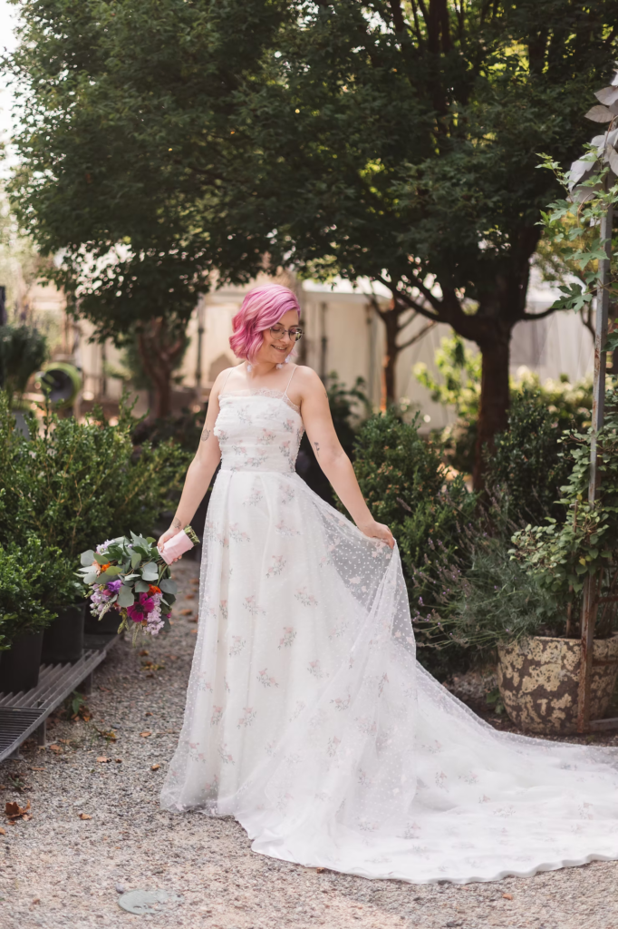 Bridal portrait at Terrain in Glen Mills, PA taken in the garden. She wears a white dress with pink flowers and her hair is a matching shade of pink. She holds a colorful bouquet. Taken by philly wedding photographer Madison Neumann Photography.