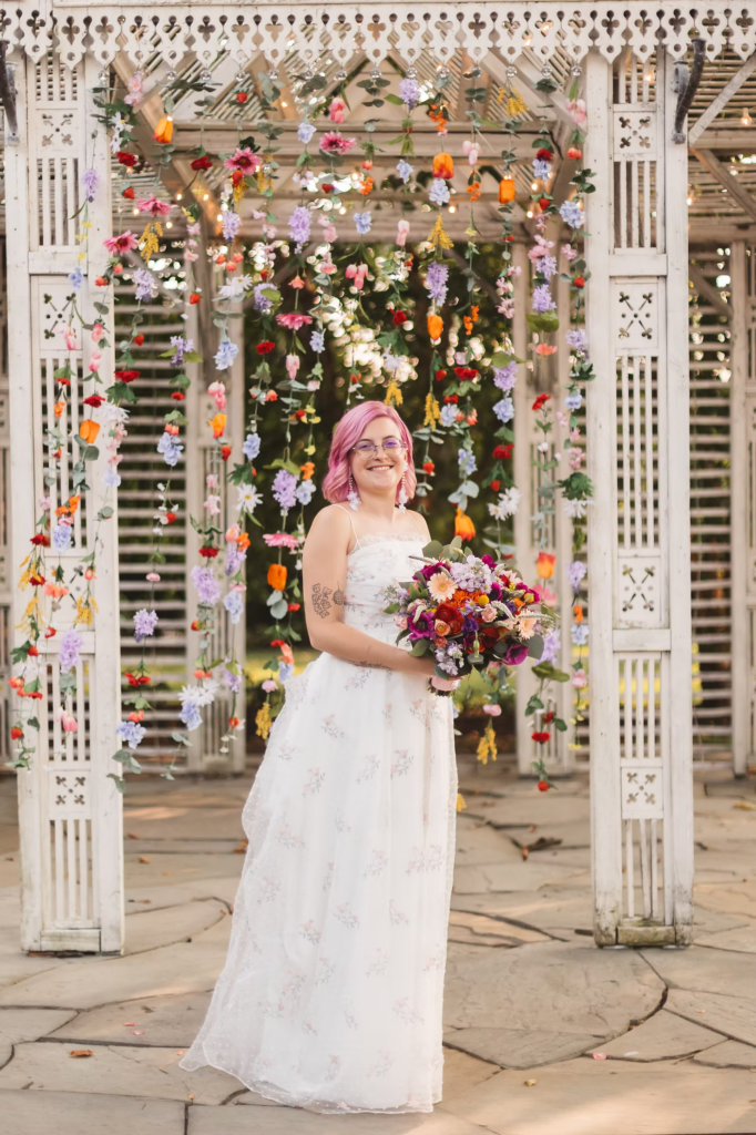Bride poses in front of handmade backdrop on her wedding day at Terrain Glen Mills, PA.
