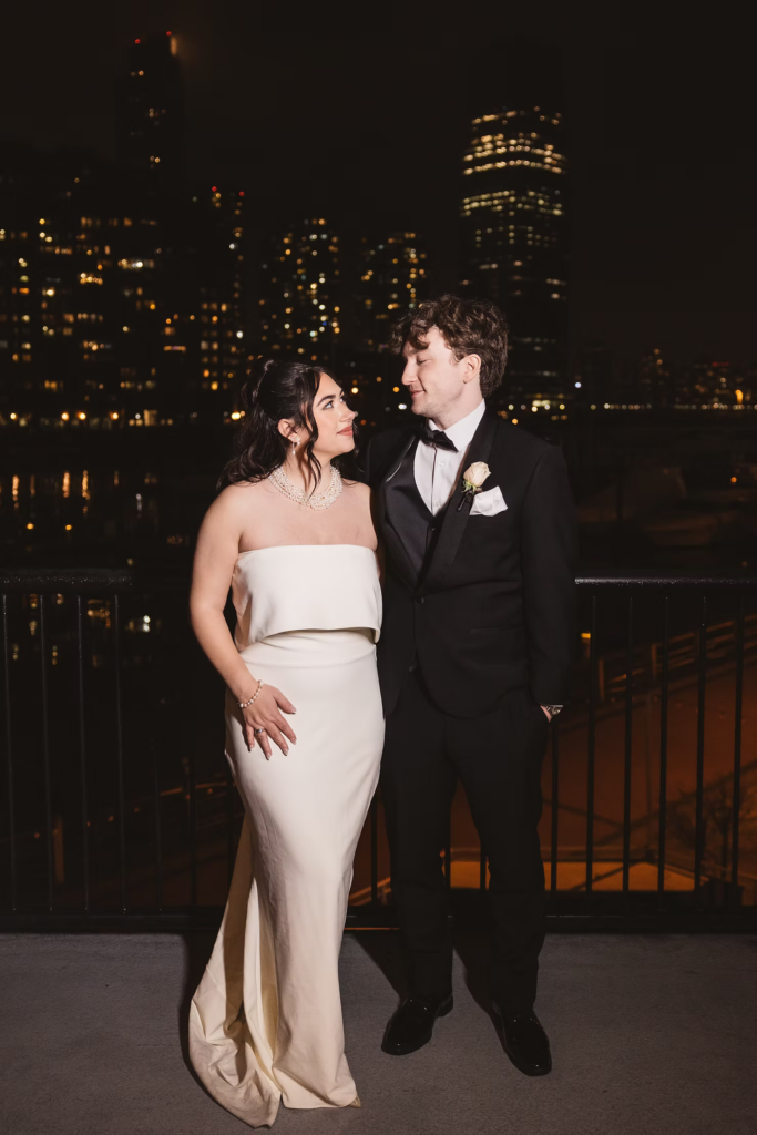 Nighttime portrait of newlywed bride and groom with city behind them. Wedding day at Maritime Parc in Jersey City, NJ. Photographed by South Jersey, Philadelphia based wedding photographer Madison Neumann Photography.