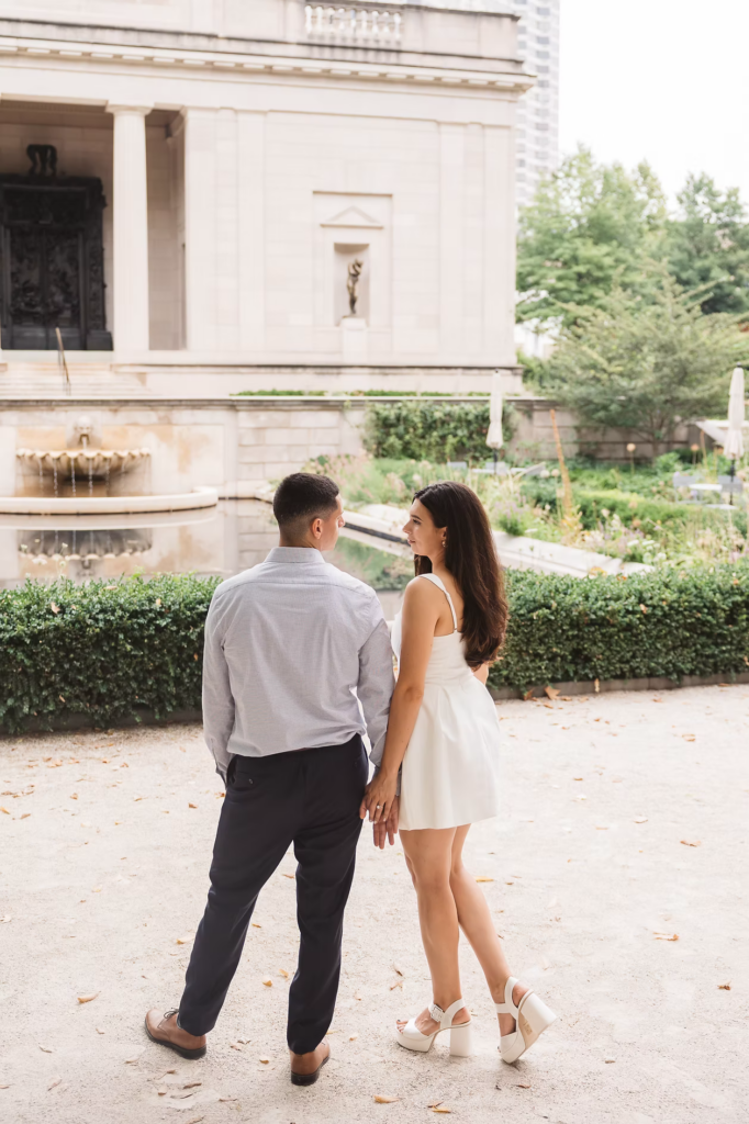 Future bride and groom look at each other by a fountain in the garden of The Rodin Museum in Philadelphia, PA. Photographed by Philly, South Jersey region wedding photographer Madison Neumann Photography.