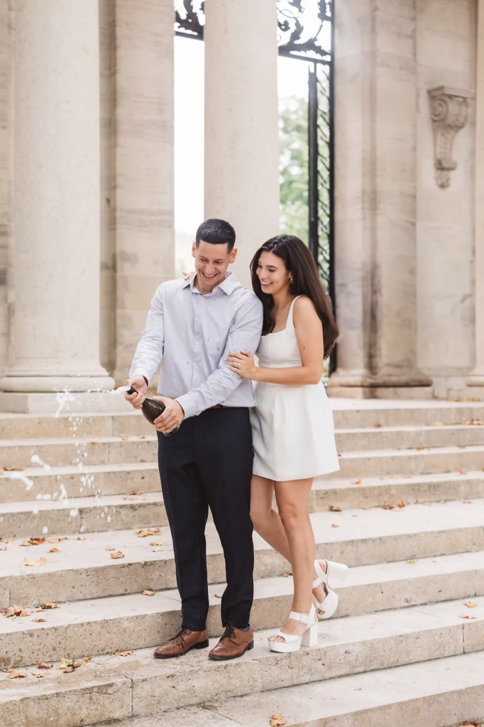 Fiancées pop champagne bottle on steps outside of The Rodin Museum in Philadelphia, PA to celebrate their engagement. Photographed by Philly, South Jersey region wedding photographer Madison Neumann Photography.