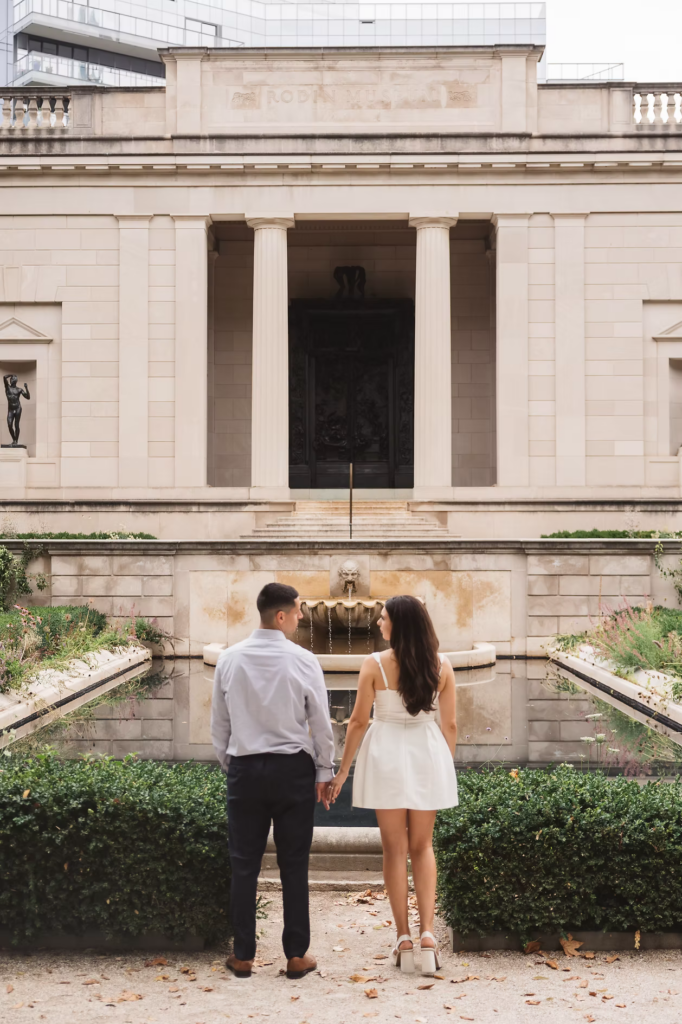 Future bride and groom hold hands in front of water fountain in the garden of The Rodin Museum in Philadelphia, PA. Engagement session photographed by Philly, South Jersey based wedding photographer Madison Neumann Photography.