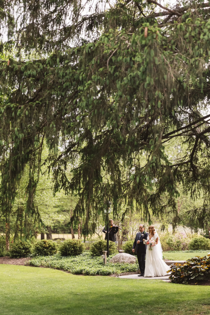 Bride walks down the aisle under trees and greenery for Pennsylvania wedding in the Pocono Mountains. Photographed by South Jersey Philly Wedding Photographer Madison Neumann Photography.