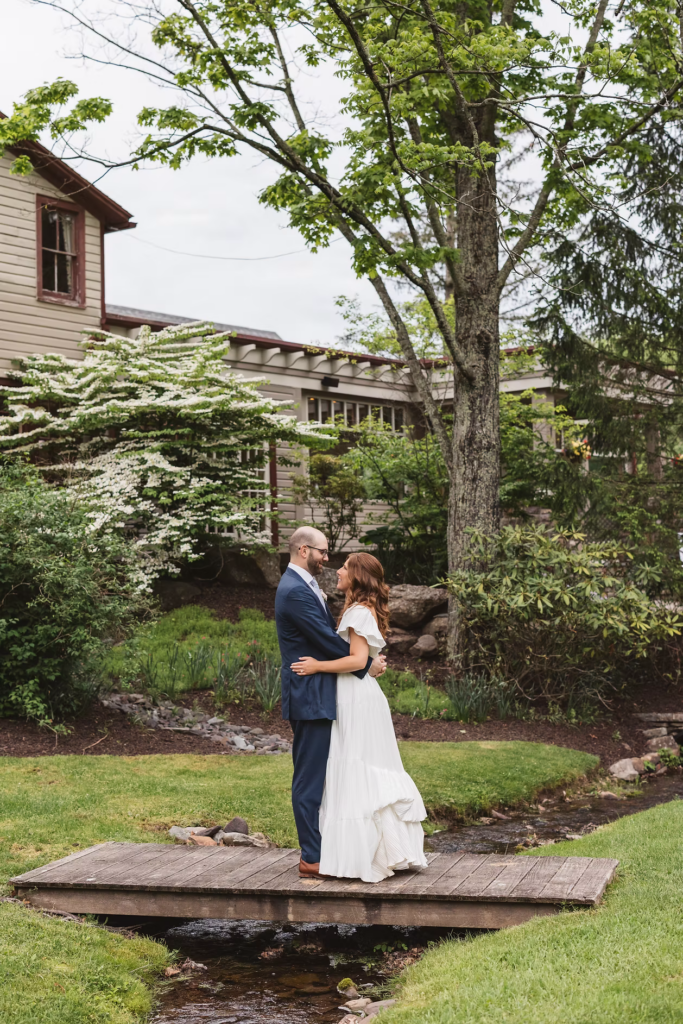 Bride and groom embrace on bridge above stream for Pennsylvania wedding in the Pocono Mountains. Photographed by South Jersey Philly Wedding Photographer Madison Neumann Photography.