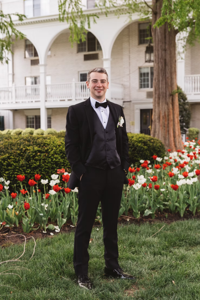 Groom smiles wearing full black suit standing in front of venue on his wedding day. Photographed at The Madison Hotel in Morristown, NJ by wedding photographer Madison Neumann Photography.
