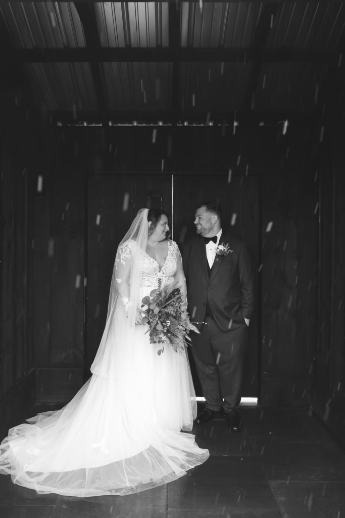 Snow falling at Terrain Gardens at DelVal in Doylestown, Pennsylvania. Bride and groom smile together on their wedding day, photographed by South Jersey, Philadelphia based wedding photographer Madison Neumann Photography.