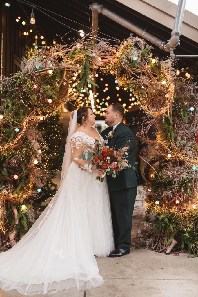 Bride and groom under archway of greenery and string lights at Terrain Gardens at DelVal in Doylestown, Pennsylvania. Photographed by South Jersey, Philly based wedding photographer Madison Neumann Photography.