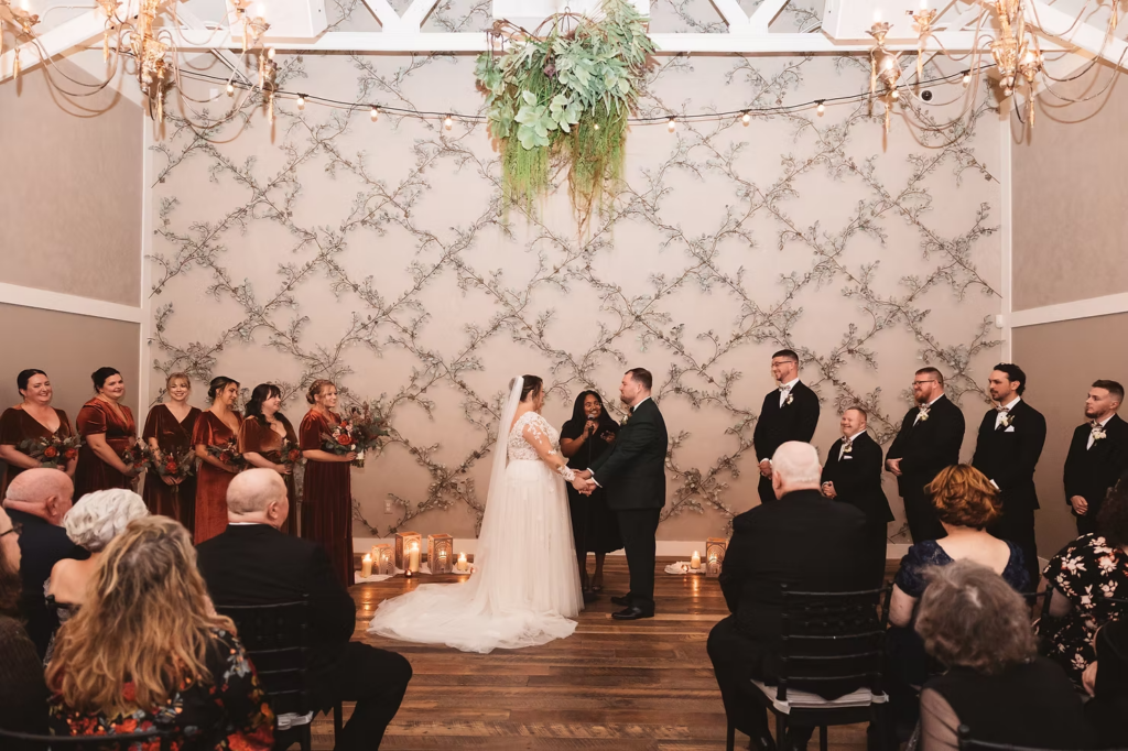 Bride and groom hold hands at the altar during indoor wedding ceremony at Terrain Gardens at DelVal in Doylestown, Pennsylvania. Photographed by South Jersey, Philadelphia based wedding photographer Madison Neumann Photography.