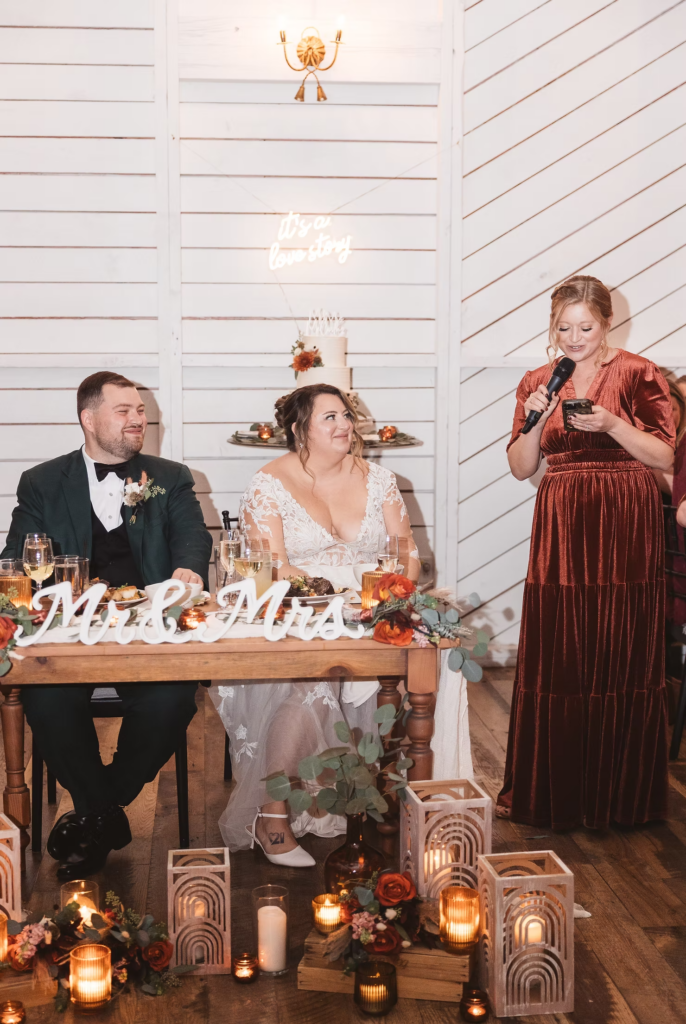 Bride and groom sit at sweetheart table during reception and listen to speeches given by wedding party. Wedding day at Terrain Gardens at DelVal in Doylestown, PA, photographed by South Jersey, Philly based wedding photographer Madison Neumann Photography.
