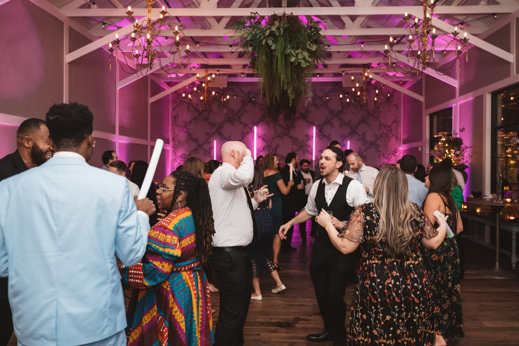 Guests dance under purple lighting on dance floor at Terrain Gardens at DelVal in Doylestown, Pennsylvania. Photographed by South Jersey, Philadelphia based wedding photographer Madison Neumann Photography.