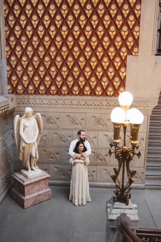 A future bride and groom pose together next to a sculpture in the halls of the Pennsylvania Academy of The Fine Arts for their art museum engagement session in Philadelphia. Photographed by Philly wedding photographer Madison Neumann Photography.