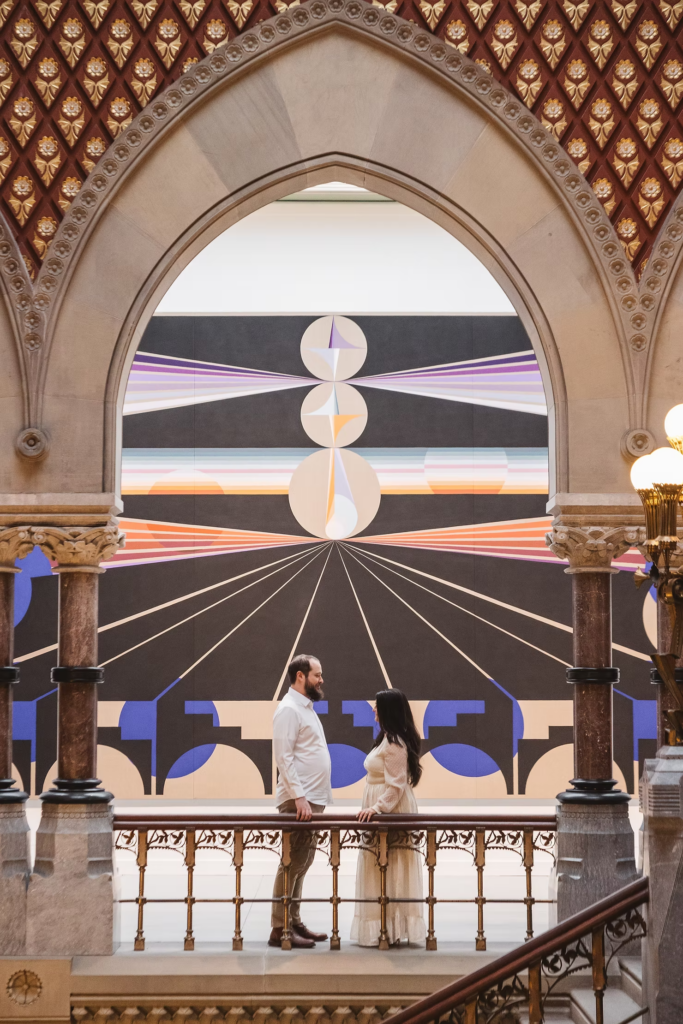 A future bride and groom pose together in front of art piece in the halls of the Pennsylvania Academy of The Fine Arts for their art museum engagement session in Philadelphia. Taken by Philly wedding photographer Madison Neumann Photography.