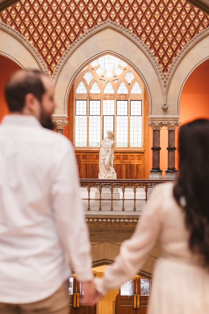 A future bride and groom hold hands and look at sculpture together at the Pennsylvania Academy of The Fine Arts for their art museum engagement session in Philadelphia. Photographed by Philly wedding photographer Madison Neumann Photography.