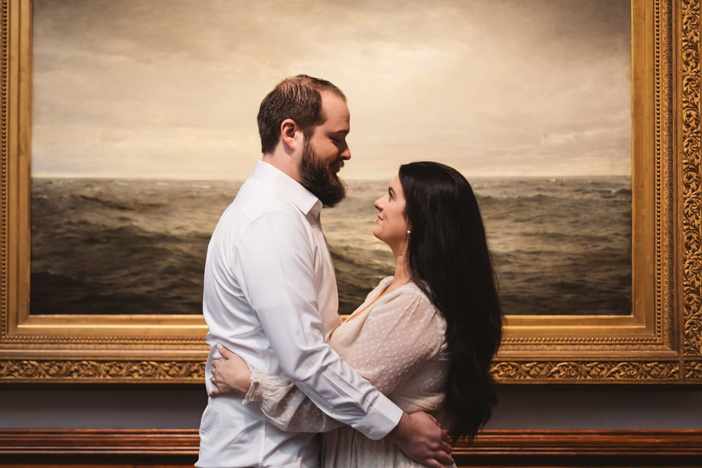 A future bride and groom smile and look at one another in front of a painting at the Pennsylvania Academy of The Fine Arts for their art museum engagement session in Philadelphia. Photographed by Philly photographer Madison Neumann Photography.