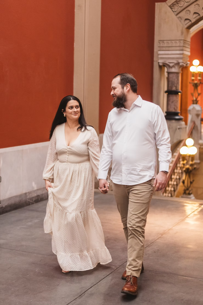 A future bride and groom hold hands and walk together in the halls of the Pennsylvania Academy of The Fine Arts for their art museum engagement session in Philadelphia. Photographed by Philly wedding photographer Madison Neumann Photography.