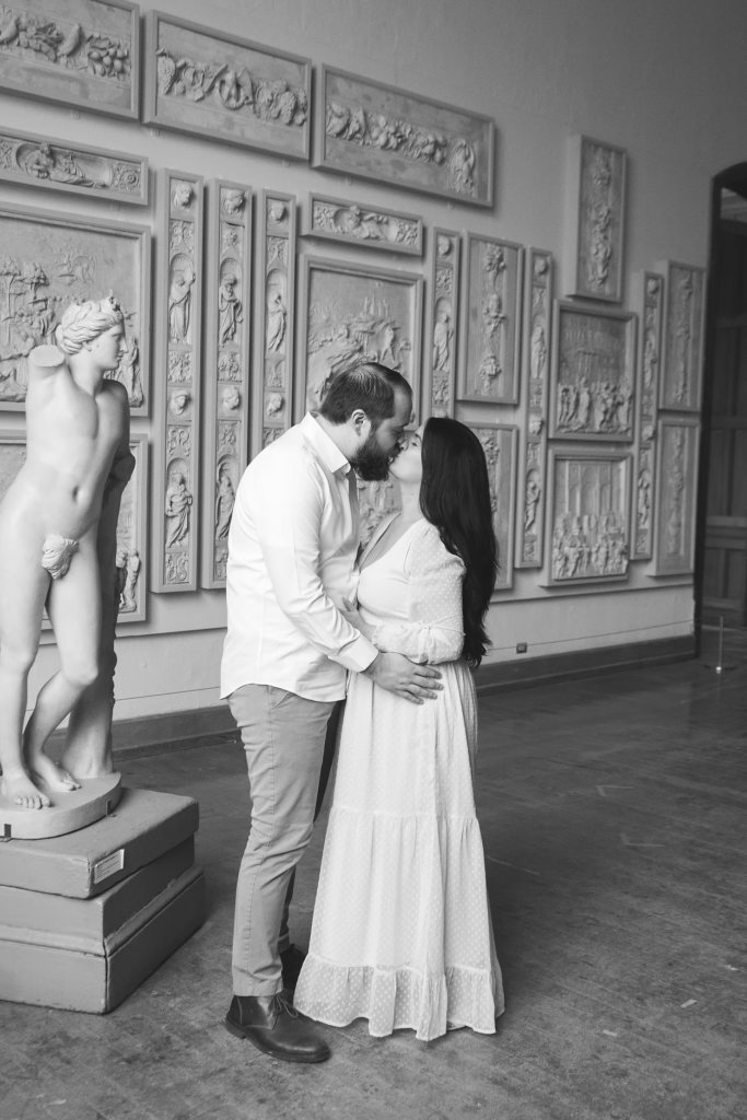A future bride and groom pose together in the halls of the Pennsylvania Academy of The Fine Arts for their art museum engagement session in Philadelphia. Behind them is a sculpture and ornate art pieces on the wall. Photographed by Philly photographer Madison Neumann Photography.