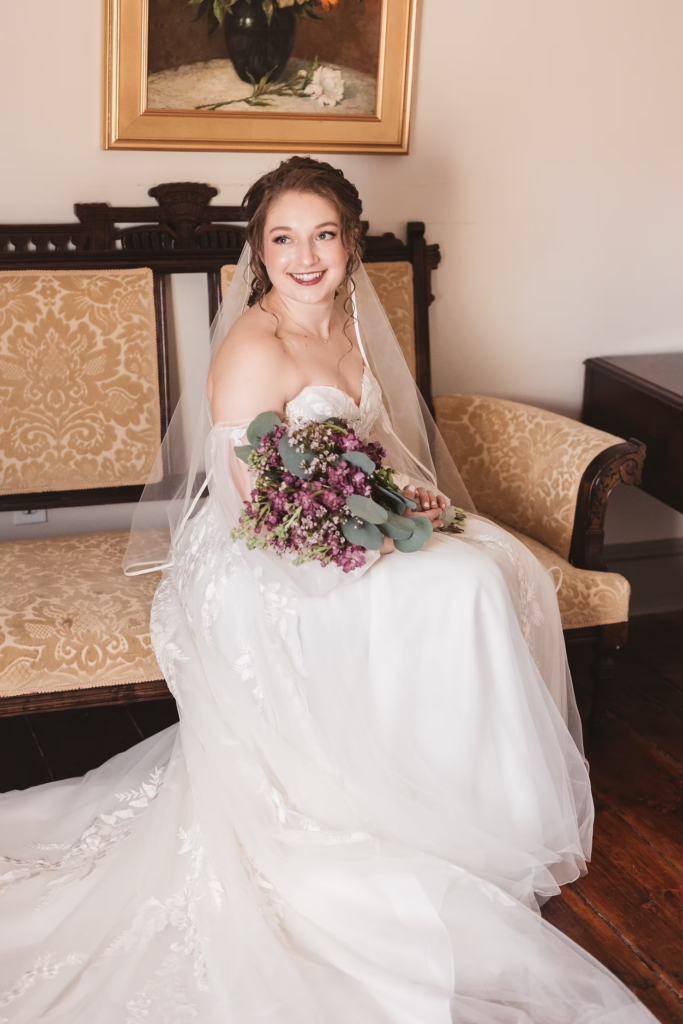 Bride in gown with long train and veil, holding purple flower bouquet, getting ready for wedding day. Photographed at David's Country Inn in Hackettstown, NJ by South Jersey, Philadelphia based wedding photographer Madison Neumann Photography.