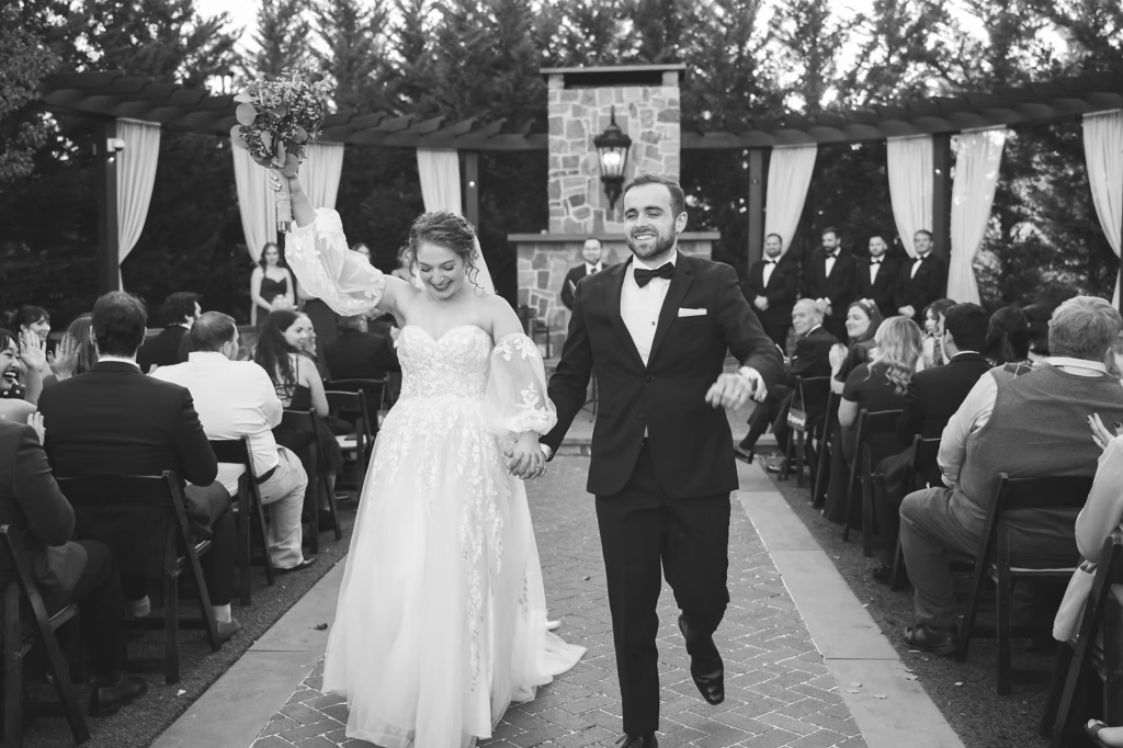 Newlywed bride and groom celebrate and walk down the aisle together after ceremony. Wedding day at at David's Country Inn in Hackettstown, NJ, outdoor ceremony in front of fireplace. Photographed by South Jersey, Philadelphia based wedding photographer Madison Neumann Photography.
