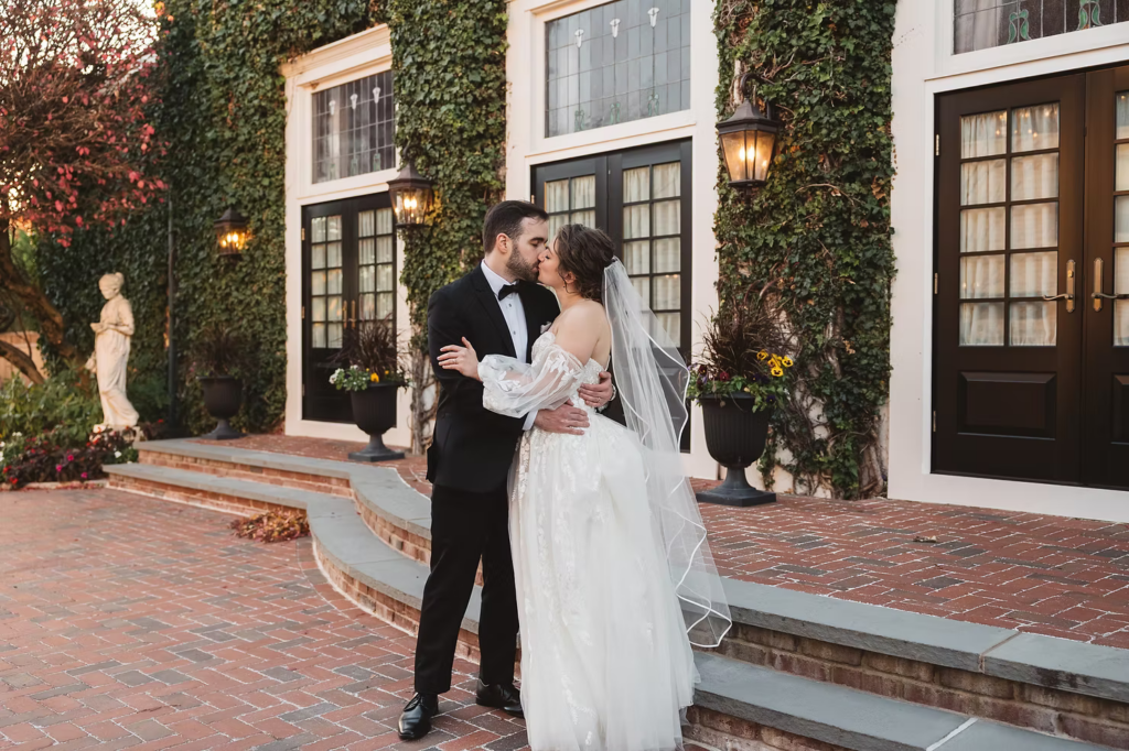 Bride and groom out front of wedding venue at David's Country Inn in Hackettstown, NJ. Ivy on walls of historic building, statue, plants and greenery. Photographed by South Jersey, Philadelphia based wedding photographer Madison Neumann Photography.