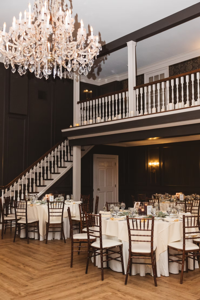 Ornate chandelier, balcony, and decorated tables with flowers and candles for wedding reception at David's Country Inn in Hackettstown, NJ. Photographed by South Jersey, Philadelphia based wedding photographer Madison Neumann Photography.