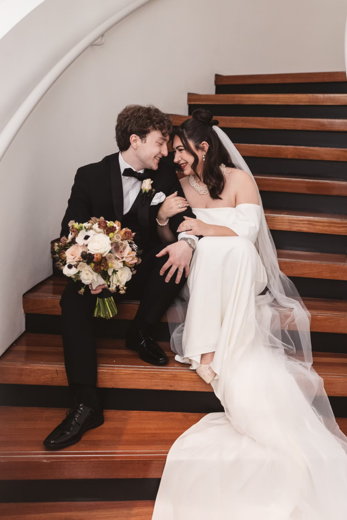 Bride and groom smile and sit together on spiral staircase. Wedding day at Maritime Parc in Jersey City, NJ. Photographed by South Jersey, Philadelphia based wedding photographer Madison Neumann Photography.