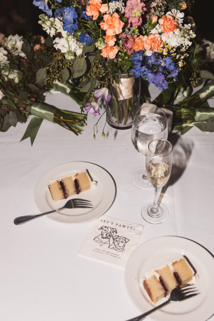 Wedding cake slices, personalized napkins, and glasses of champagne on table at reception. Wedding day at the American Swedish Historical Museum in Philadelphia, PA. Photographed by South Jersey/Philly based wedding photographer Madison Neumann Photography.