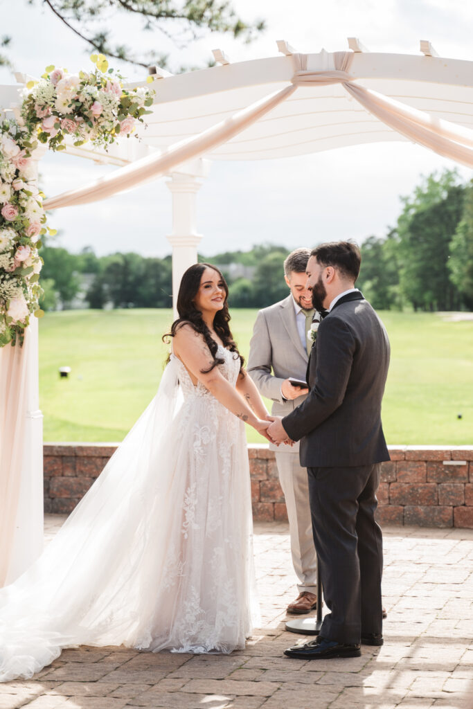Bride and groom stand together holding hands at the altar during ceremony. Wedding day at Blue Heron Pines Golf Club in Egg Harbor, NJ. Photographed by South Jersey/Philly based wedding photographer Madison Neumann Photography.