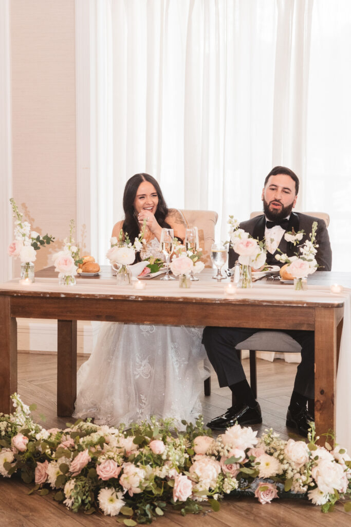 Bride and groom sitting at sweetheart table laughing. Wedding day at Blue Heron Pines Golf Club in Egg Harbor, NJ. Photographed by South Jersey/Philly based wedding photographer Madison Neumann Photography.