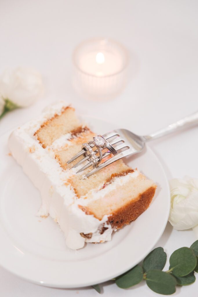 Wedding rings stacked on fork on top of slice of wedding cake. Wedding day at Blue Heron Pines Golf Club in Egg Harbor, NJ. Photographed by South Jersey/Philly based wedding photographer Madison Neumann Photography.