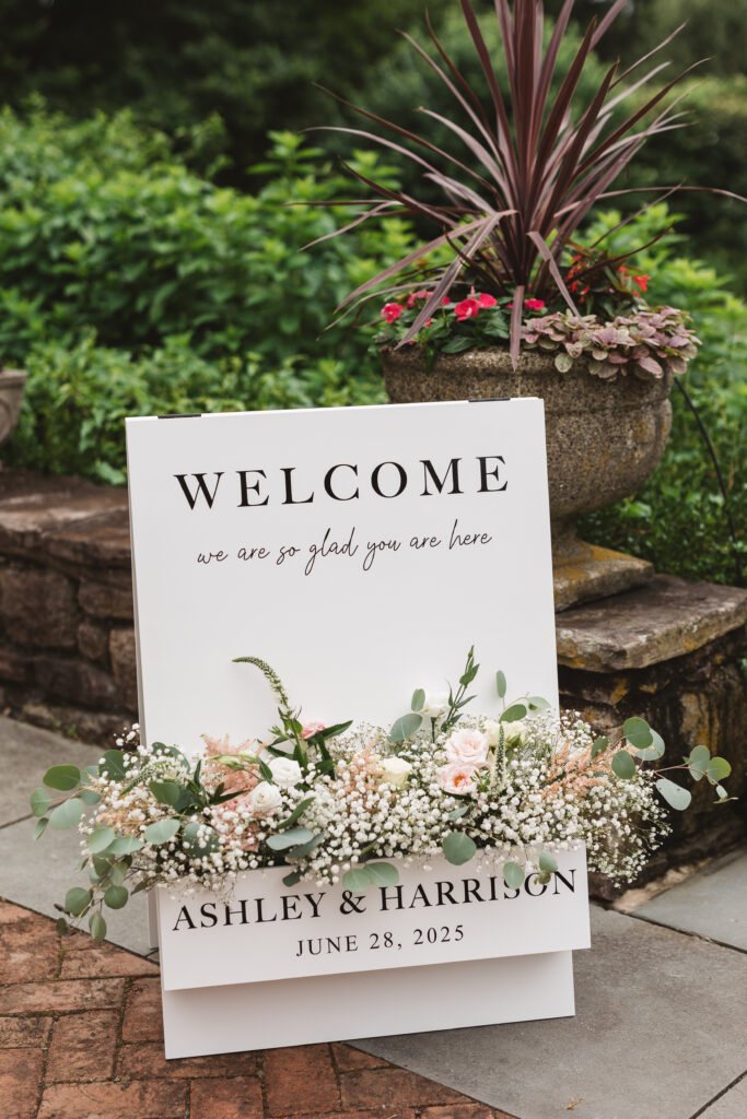Sign welcoming guests as they walk to their seats for the ceremony in the garden at Woolverton Inn, photographed by New Jersey and Philadelphia based travel wedding photographer Madison Neumann Photography.